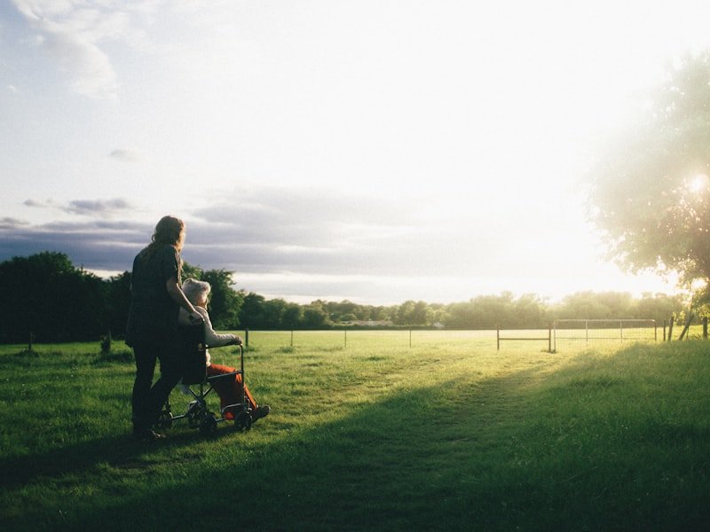 A caregiver walking alongside a senior in a wheelchair on a peaceful path