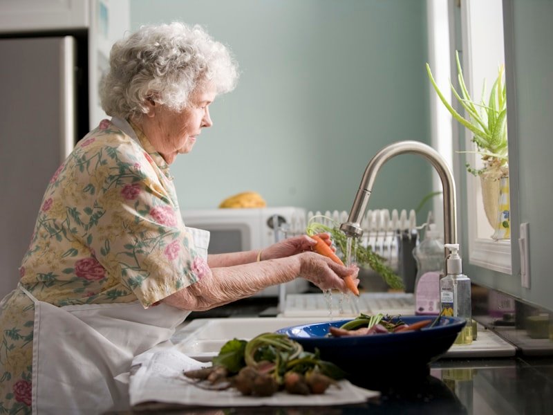A senior comfortably back in her own kitchen washing fresh vegetables