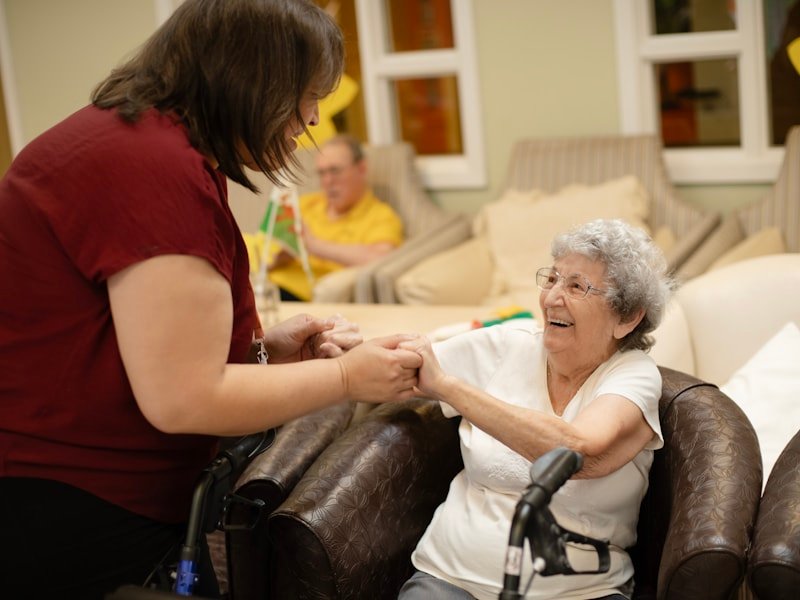 A caregiver helping a senior up from her chair with a walker beside her